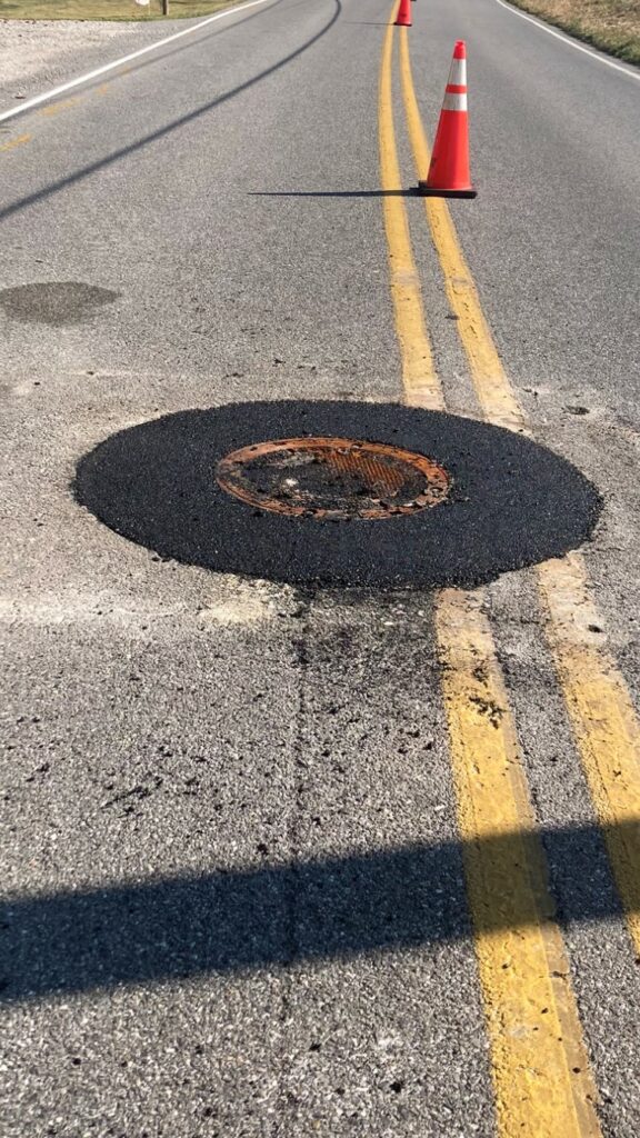 Middle of the street focused on a manhole cover that has been repaired to the same grade as the street.