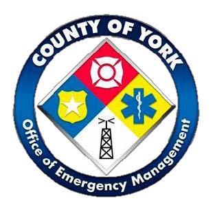 A circular blue logo with a white inner ring. Around the ring are the words “County of York” at the top and “Office of Emergency Management” at the bottom in white capital letters. Inside, a white circle contains a diamond divided into four quadrants: The top quadrant is red and shows a white all‑hazards emblem. The left quadrant is blue and features a yellow sheriff’s star badge. The right quadrant is yellow and displays a blue Star of Life medical symbol. The bottom quadrant is white and depicts a black radio communications tower.