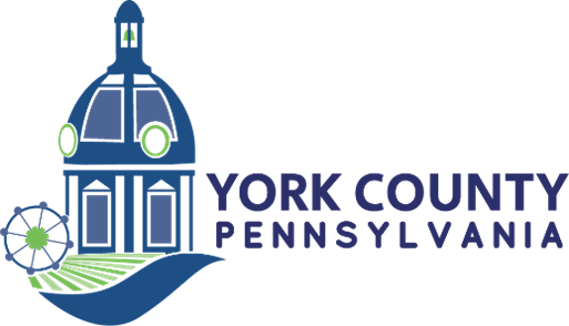 Logo of York County, Pennsylvania, featuring a blue and green illustration of a domed courthouse building with circular details, a ferris wheel on the left, and stylized farmland at the bottom. The text 'York County Pennsylvania' is written to the right.